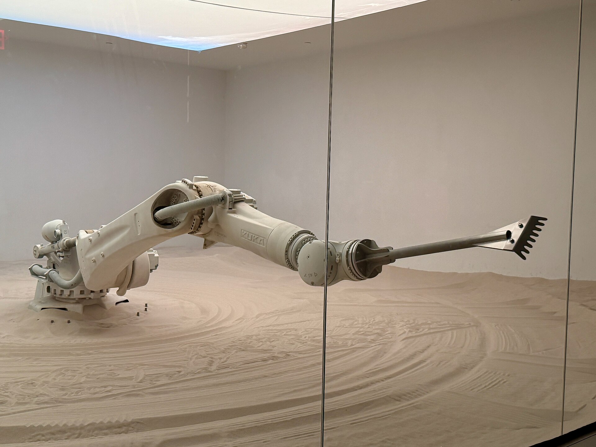 White industrial robot arm drawing patterns in sand